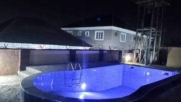 Une piscine avec un escalier, entourée d’une maison protégée par une clôture en fil de fer barbelé.