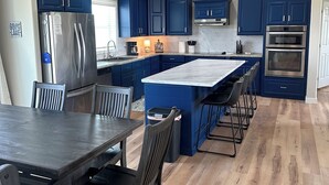 A modern kitchen with blue cabinets, stainless steel appliances, and a wooden dining table. - The Reel Deal in Devils Lake with Shop – Boat Launch Nearby (Devils Lake)