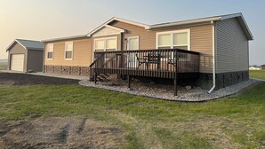 A single-story mobile home with a covered porch, a garage, and a small adjacent shed. - The Reel Deal in Devils Lake with Shop – Boat Launch Nearby (Devils Lake)