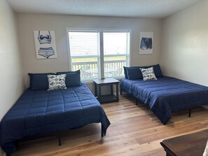 Un dormitorio con dos camas individuales, una mesita pequeña y una ventana con persianas.