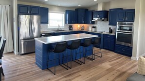 A modern kitchen with blue cabinets, stainless steel appliances, and a central island with bar stools. - The Reel Deal in Devils Lake with Shop – Boat Launch Nearby (Devils Lake)