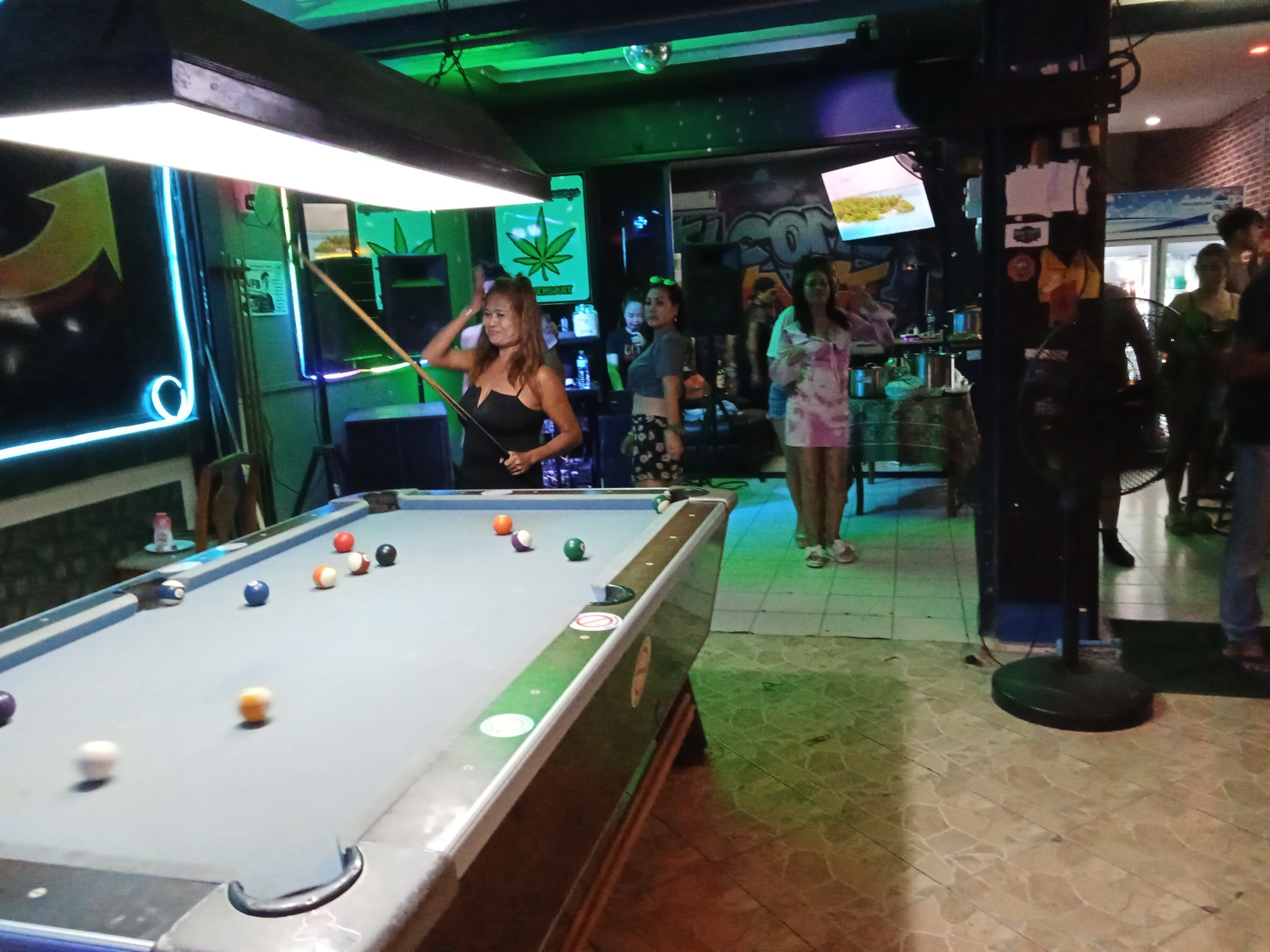 A pool table with balls, a neon sign, and a brick wall.