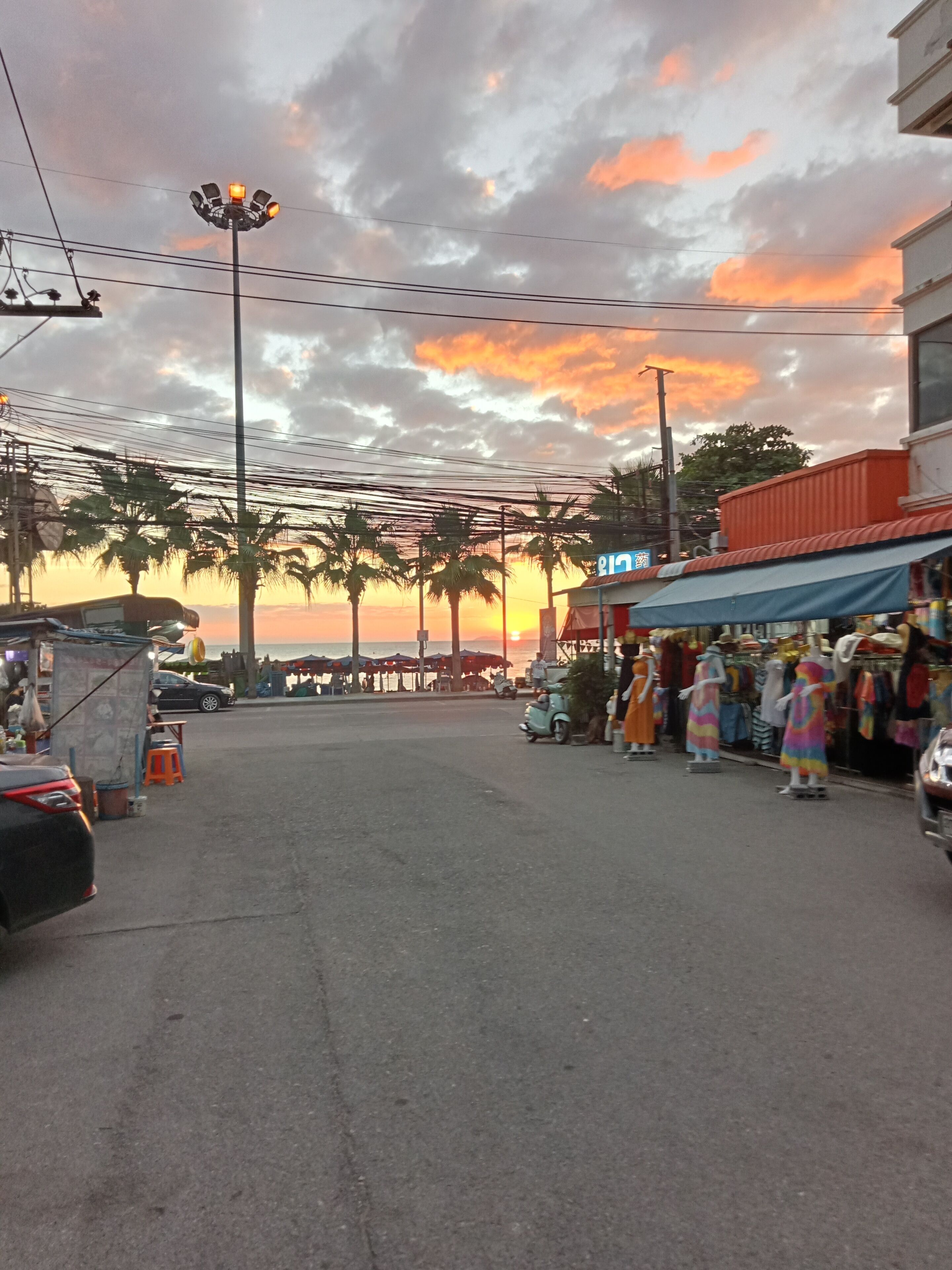 A street scene with a sunset, palm trees, and a market area with clothing stalls.