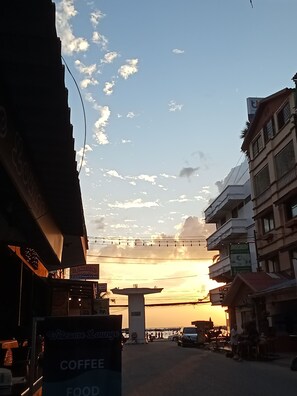 A street view with a prominent tower structure in the center, surrounded by various buildings and signs, including a coffee shop and a restaurant. - Welcome Lounge Jomtien (Pattaya)