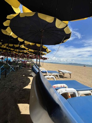 A beach with rows of sun loungers and umbrellas providing shade.