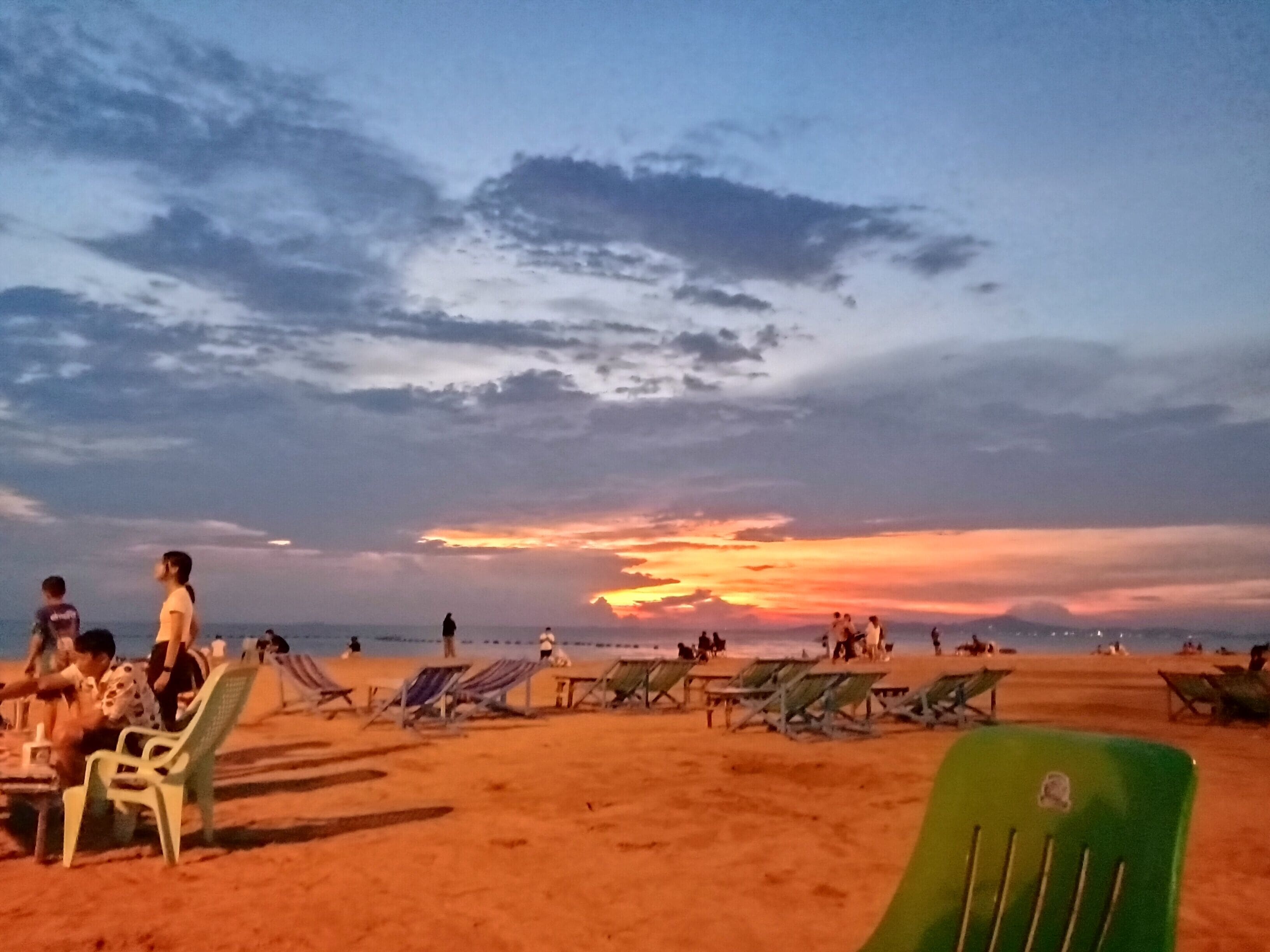 Ein Strand mit mehreren Reihen von Liegestühlen und Sonnenschirmen, sowie entspannte Menschen.