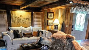 Un interior rústico con techo de madera, un sofá blanco, un tapete rojo y una estatua de oso apoyada en un pilar de ladrillo.
