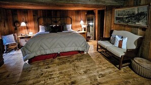 Un dormitorio rústico con una cama grande, cabecera de madera, una silla y un cuadro en la pared.