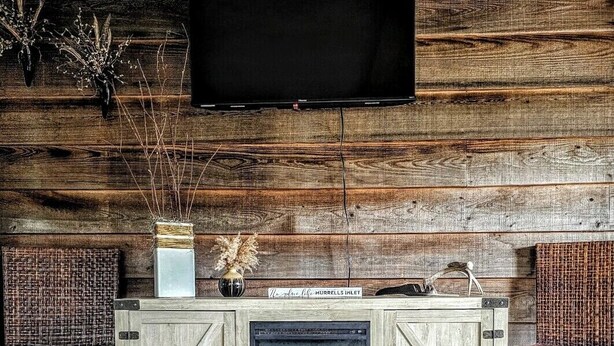 Una sala de estar rústica con chimenea, muebles de madera y un televisor de pantalla plana montado en una pared de madera.