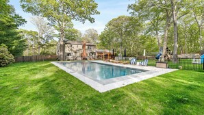 Et rektangulært swimmingpool med en omgivende træterrasse, et legetårn i træ og et hus i baggrunden.