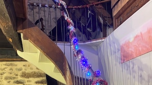 A spiral staircase with metal railings and a wooden handrail, decorated with blue and red tinsel. - 16th century thatched house, relaxation area for adults and children (Saint-Augustin)
