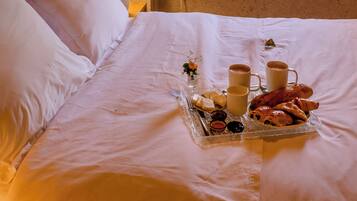 A bed with white linens, a tray of breakfast items, and a window with a view of greenery.