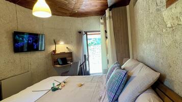 A bedroom with a wooden ceiling, a bed with white linens, a television on the wall, and a window with curtains.