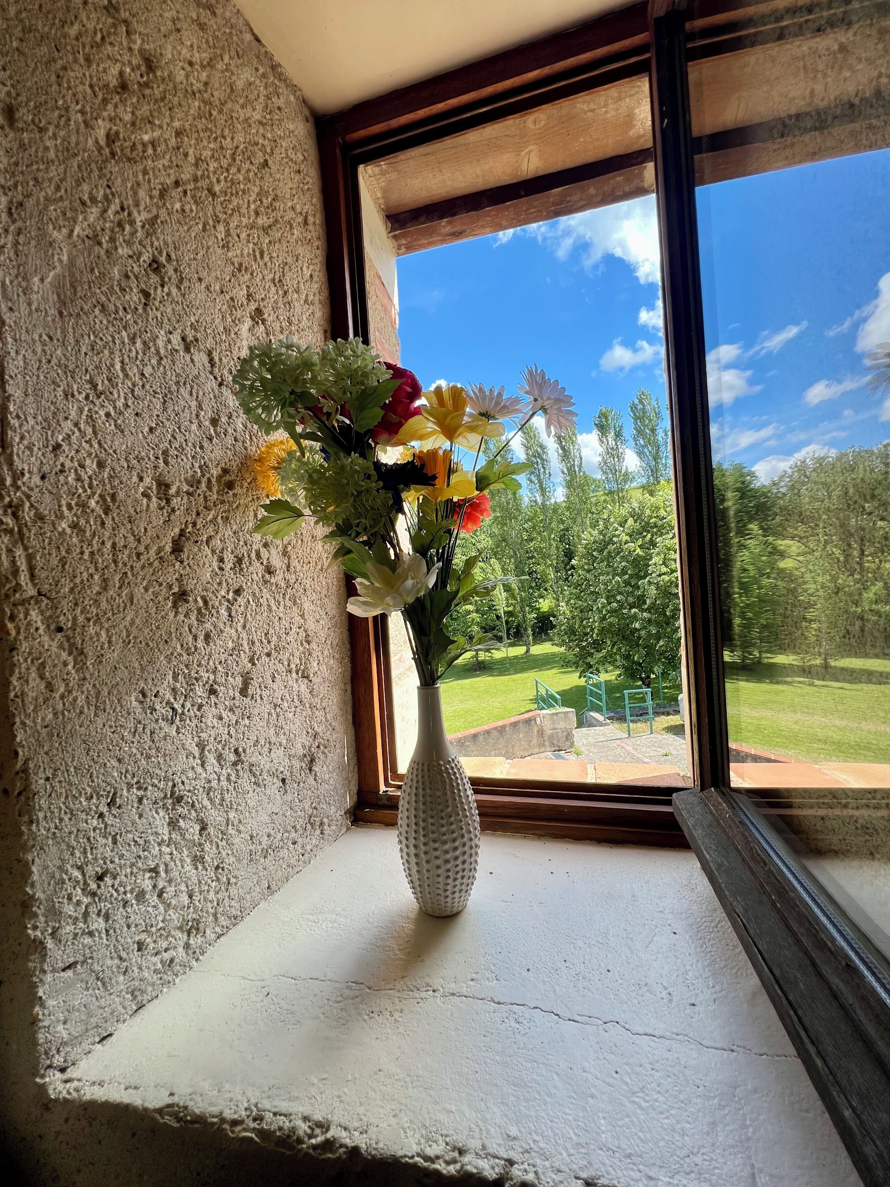 A window with a textured wall and a white vase with flowers on a ledge.