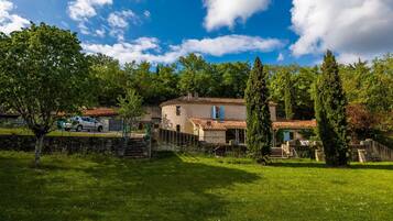 A rustic house with a stone wall, a car parked in front, and a grassy yard.