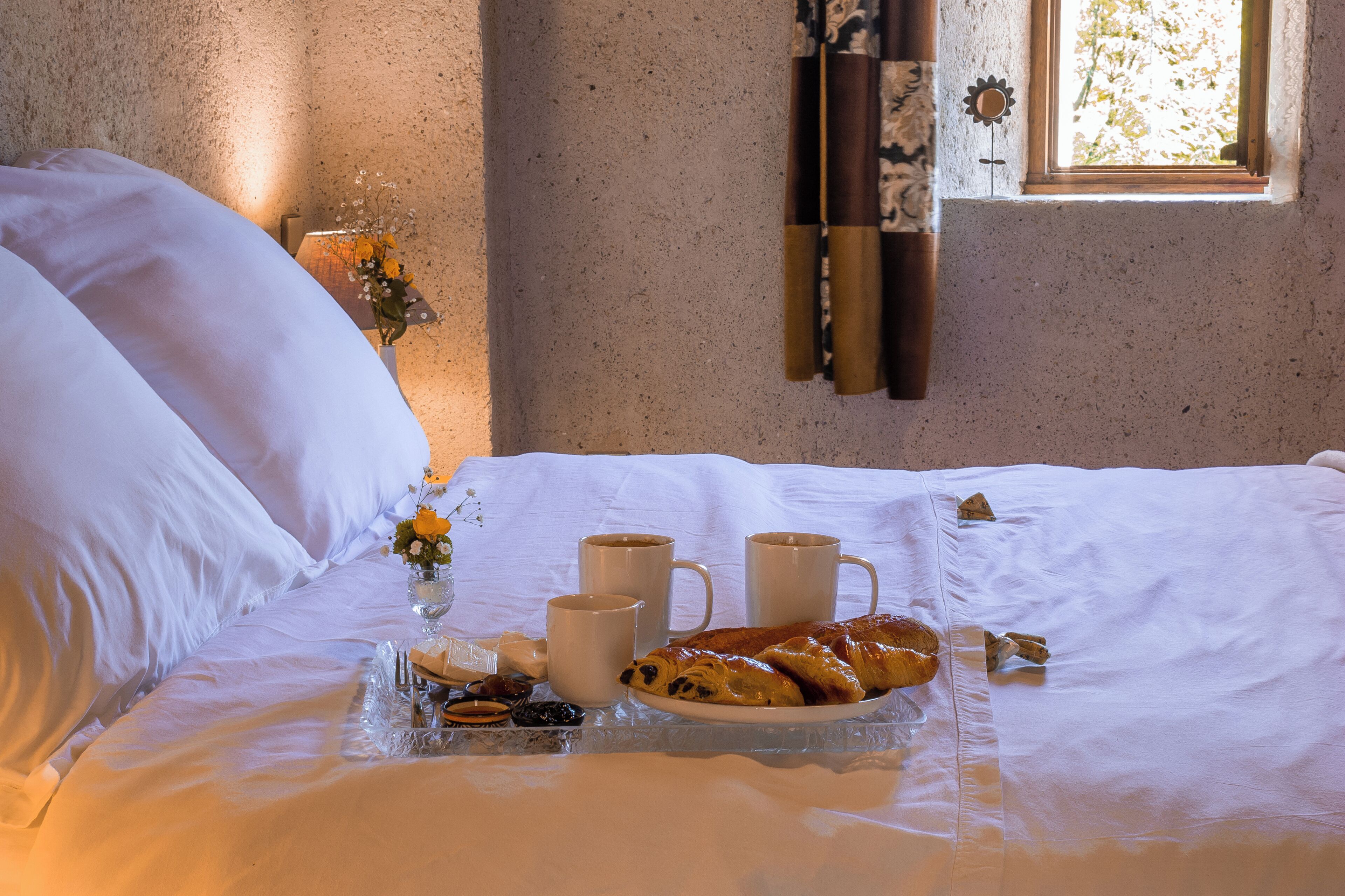 A neatly made bed with white linens, a tray with pastries, and two cups of coffee on a table.