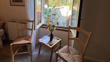 Een kamer met twee rieten stoelen, een tafeltje met een bloevas en een raam met uitzicht op een tuin.