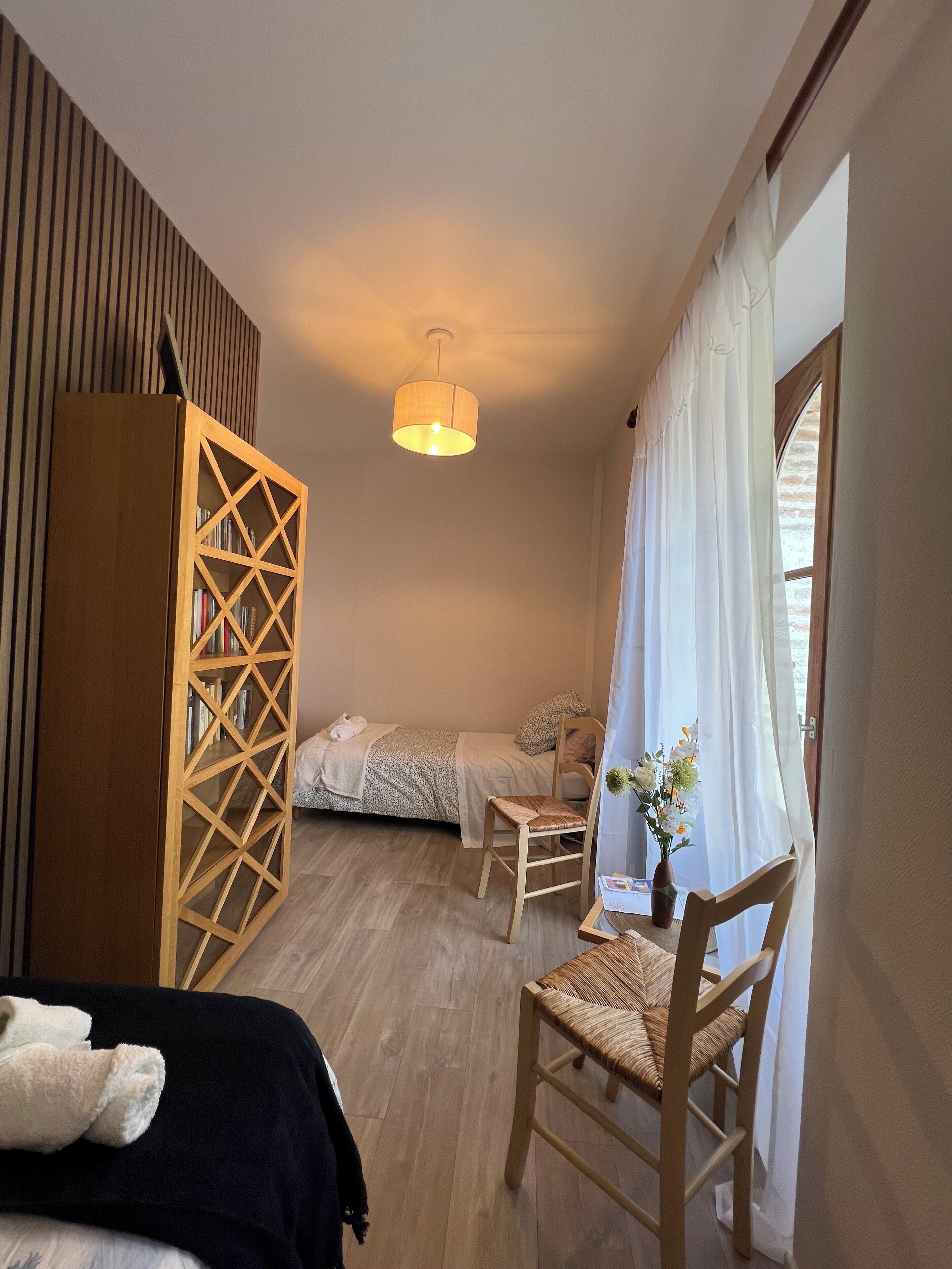 Ein Schlafzimmer mit einem Bett, einem Sessel, einem Holzschrank und einem Fenster mit Vorhängen.