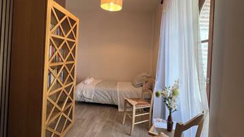 Ein Schlafzimmer mit einem Bett, einem Sessel, einem Holzschrank und einem Fenster mit Vorhängen.