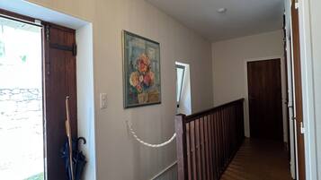 A hallway with a chandelier, a painting, and a wooden railing.