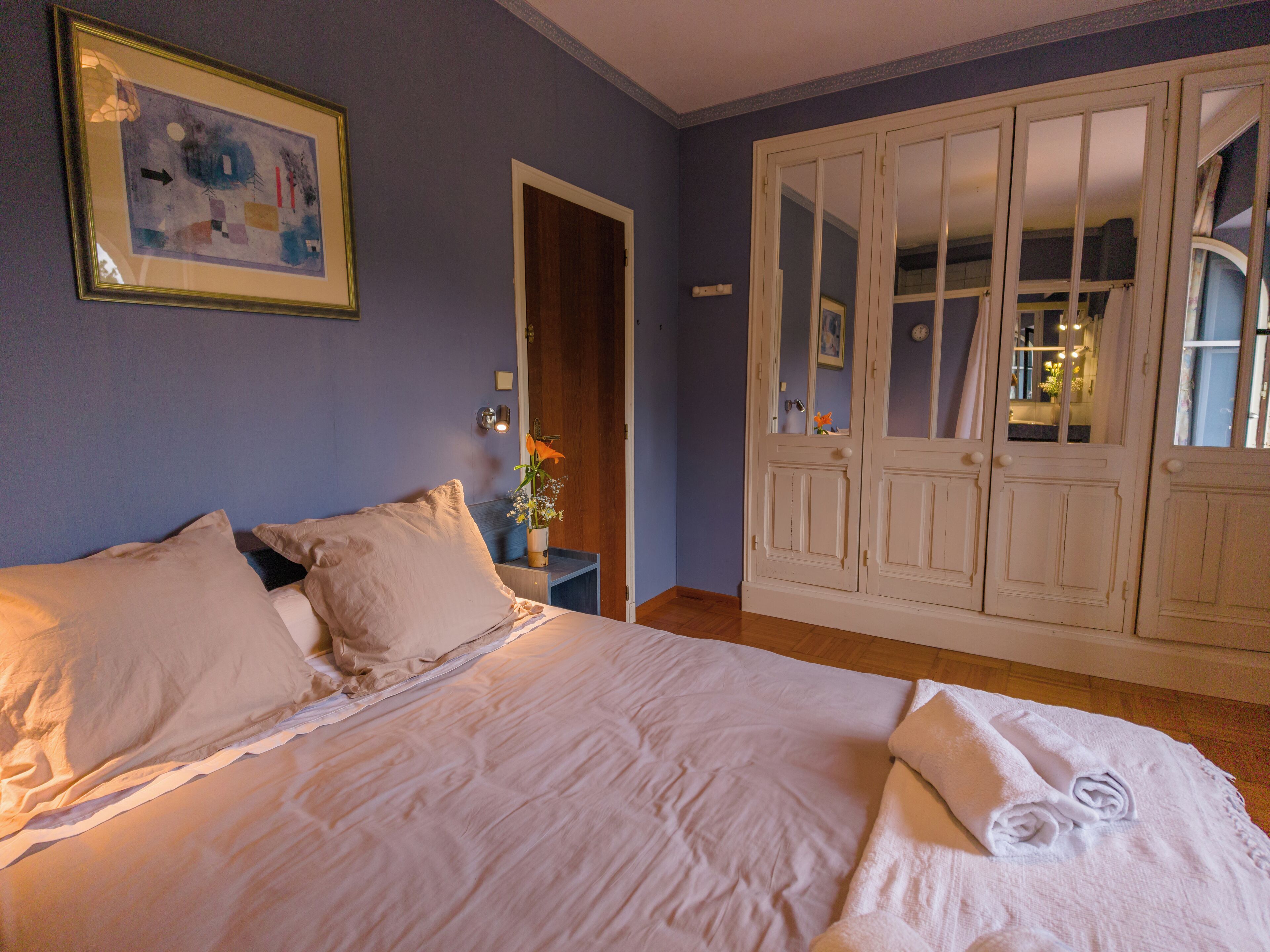 Un dormitorio con cama, mesita de noche, un jarrón con flores y un armario.
