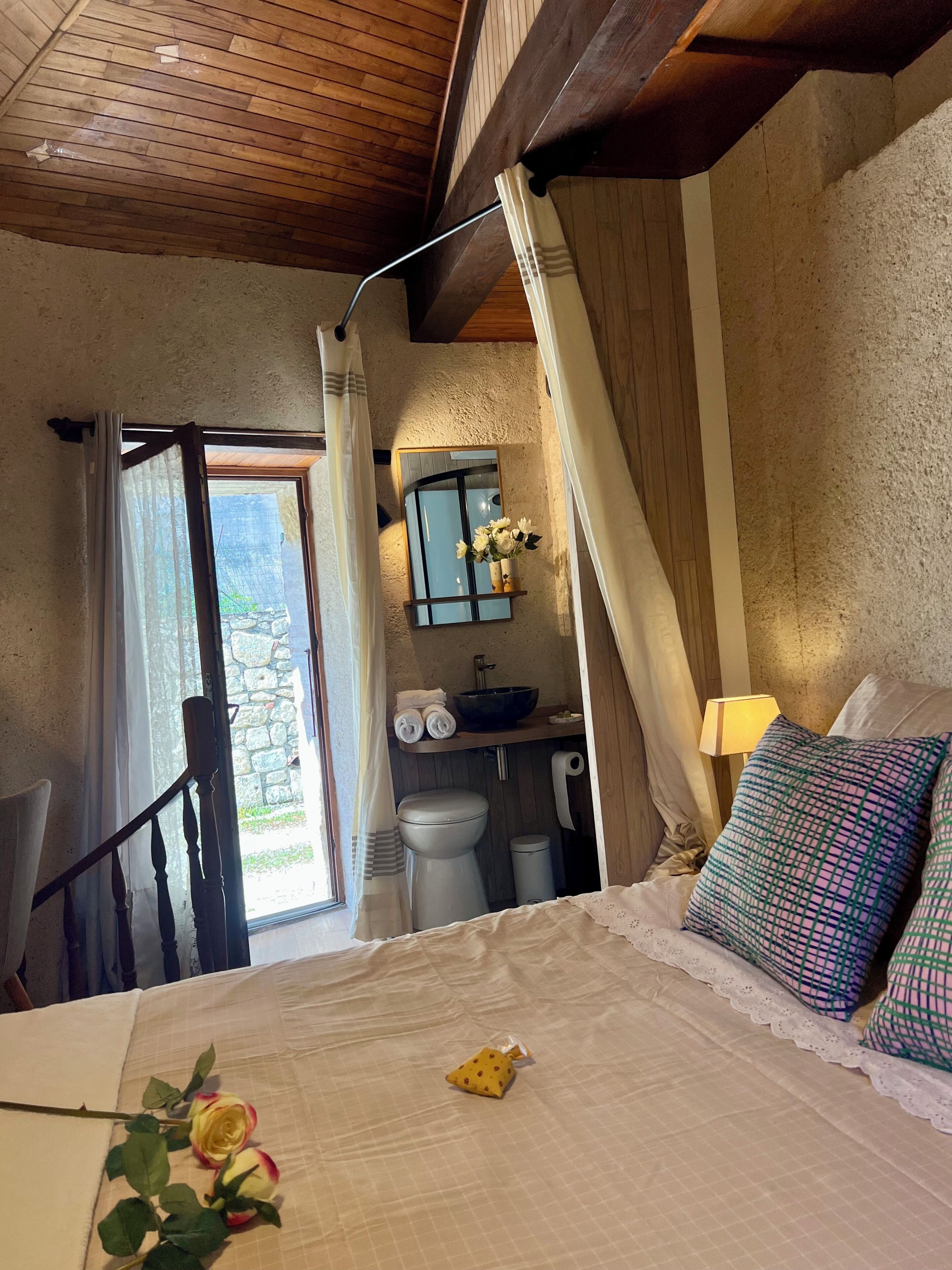 A bedroom with a bed, a window with curtains, a bathroom with a sink and toilet, and a staircase.