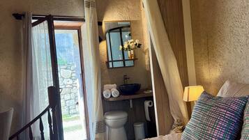 A bedroom with a bed, a window with curtains, a bathroom with a sink and toilet, and a staircase.