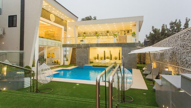 Una casa moderna con piscina, mobiliario de exterior e interior bien iluminado.