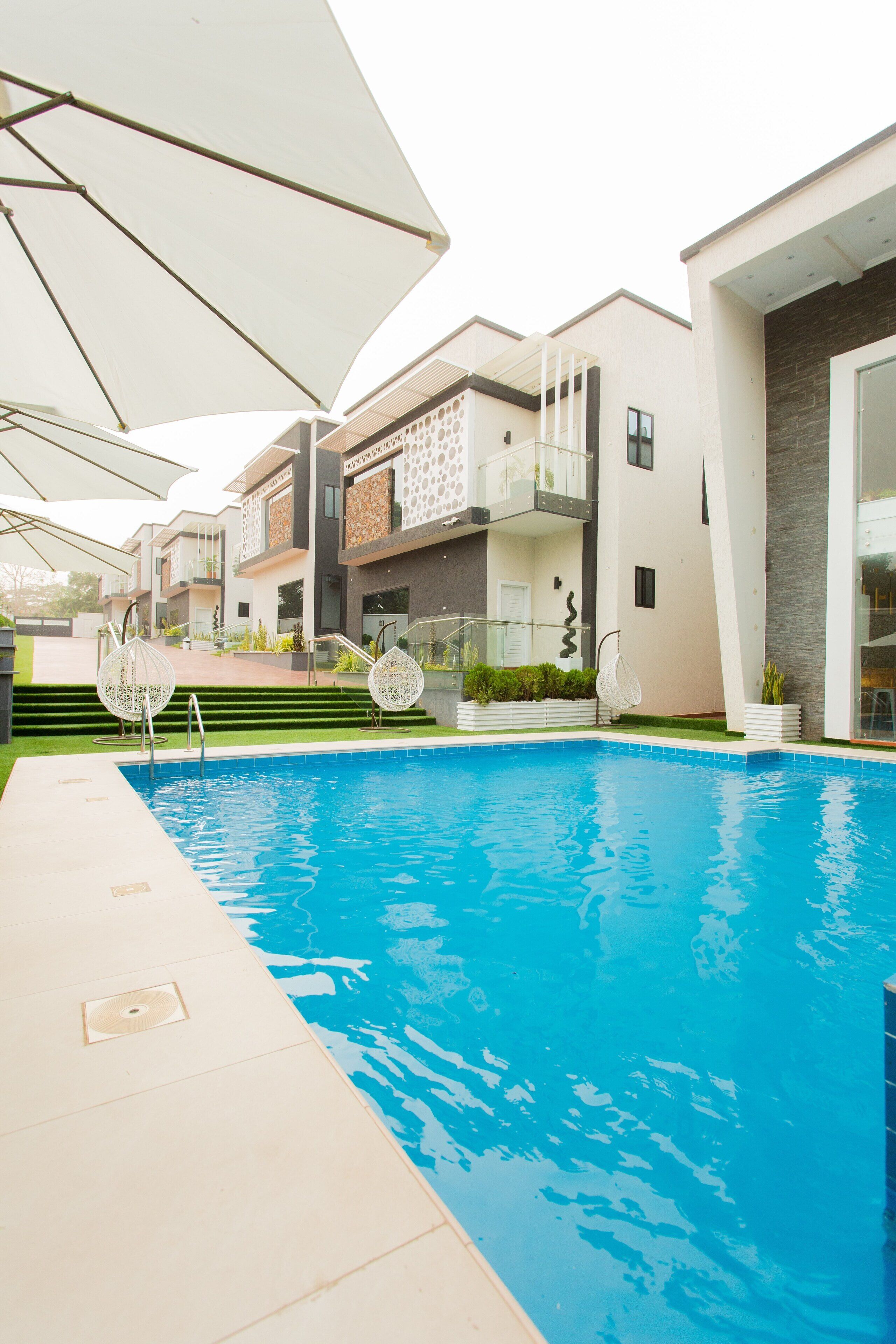 A swimming pool area with a modern building, outdoor seating, and a staircase leading to a balcony.