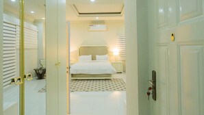 Pasillo de hotel que conduce a un dormitorio con cama, mesita de noche y velador.