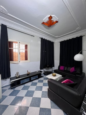 A living room with a checkered floor, a black sofa with purple cushions, a white table, and a black coffee table.
