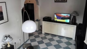 Een kamer met een geruite vloer, een witte lamp, een televisie op een kast en een lijst met een afbeelding aan de muur.