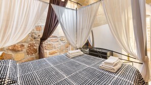 A room with a bed, white curtains, and a stone wall.