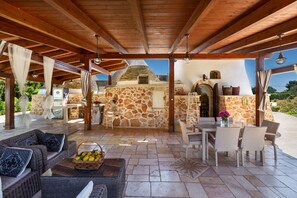 An outdoor patio with stone walls, wicker furniture, and a stone oven. - Tenuta Bouganville by Perle di Puglia (Francavilla Fontana)