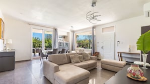 A spacious living room with a large L-shaped sofa, a dining area, and a view of the outdoors.