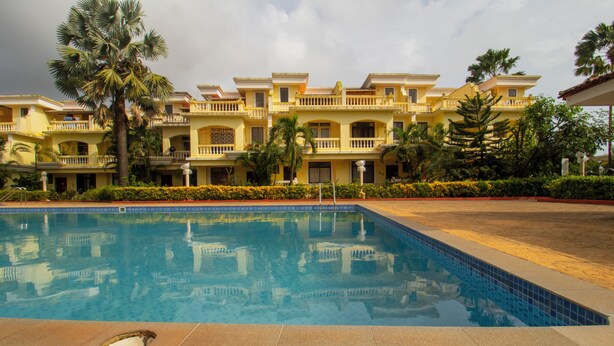 A hotel with a swimming pool, multiple balconies, and palm trees. - 5 Min to Benaulim Beach SERENE ESCAPE VILLA (Benaulim)