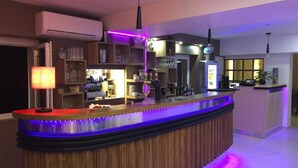 Zona bar moderna con un bancone in legno, scaffali con bicchieri e una luce al neon.