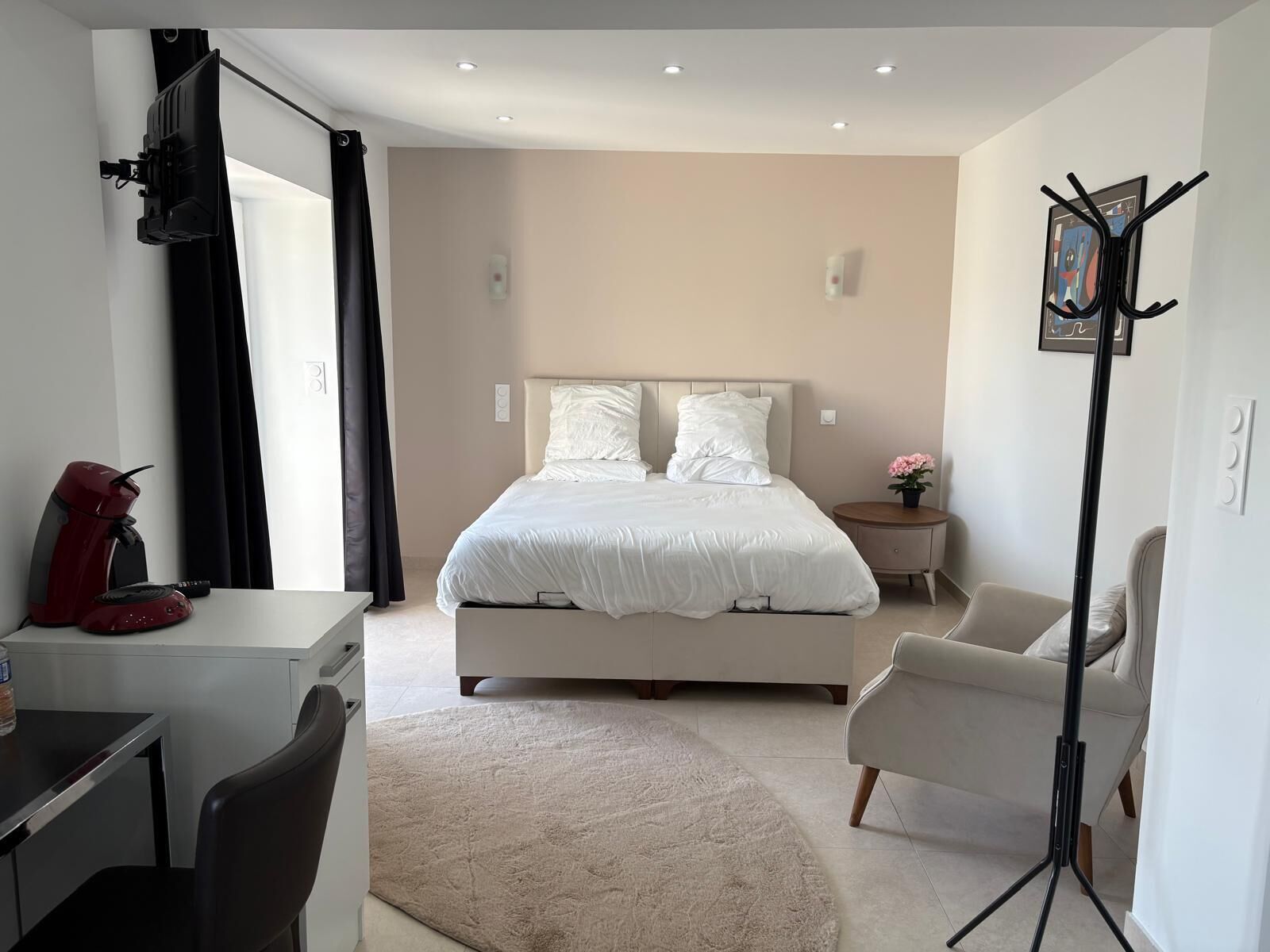 Ein modernes Schlafzimmer mit Bett, Schreibtisch, Stuhl, einer Kaffeemaschine und einer Stehlampe.