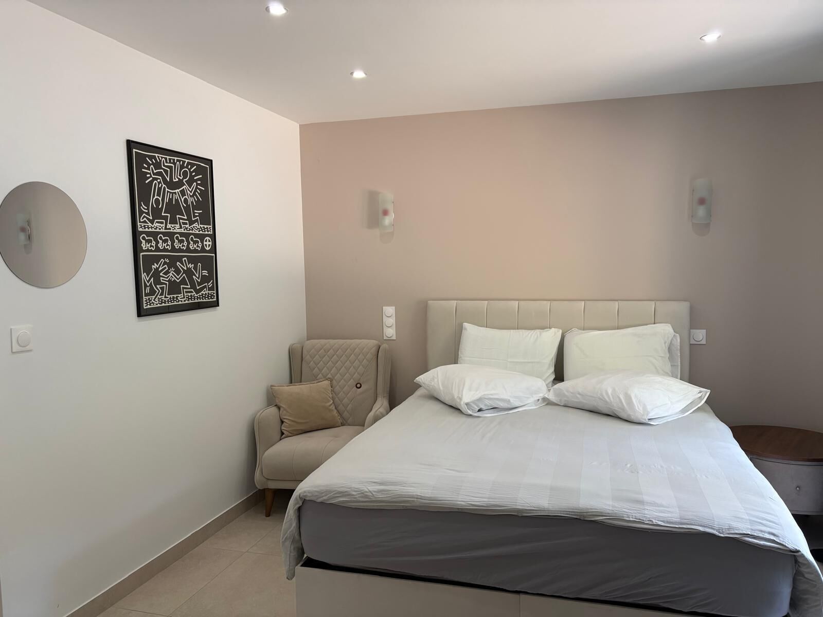 A bedroom with a bed, a chair, a wall-mounted light, and a framed picture.