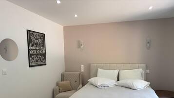 A bedroom with a bed, a chair, a wall-mounted light, and a framed picture.