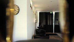 Una hall d'albergo con un orologio, un divano, una poltrona e un tavolo con una bottiglia.