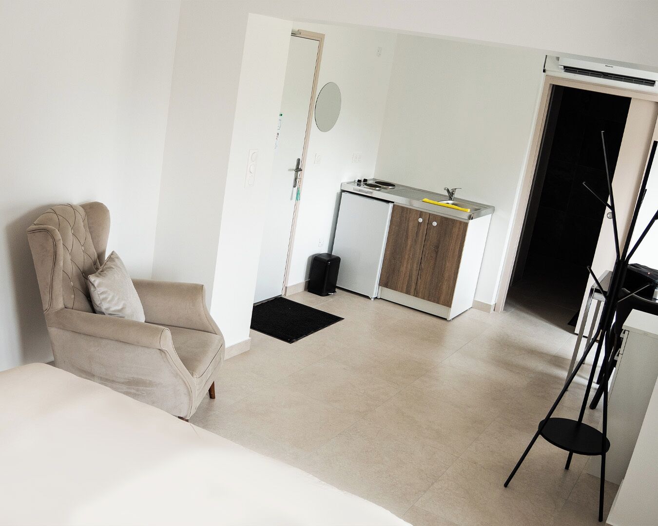 A compact room with a sofa, a kitchenette, and a door leading to another room.