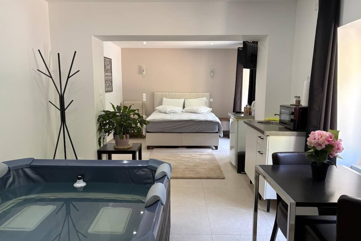 Een moderne hotelkamer met een bed, een kleine kitchenette, een eethoek en een bad.