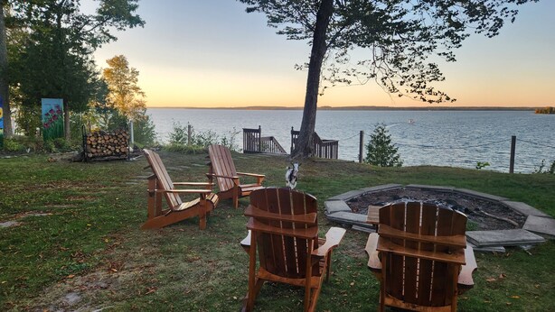 A lakeside setting with wooden Adirondack chairs, a fire pit, and a view of the lake. - Experience a 12-room historic home on Lake Manistique with your own private chef (Curtis)