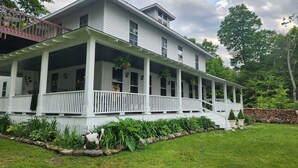A two-story white house with a covered porch, a stone wall, and a well-maintained garden. - Experience a 12-room historic home on Lake Manistique with your own private chef (Curtis)