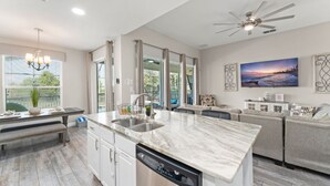 A modern kitchen with a marble countertop, built-in dishwasher, and a dining area with a bench. - Movie Theater/Game Room, FREE Pool Heat! No Rear Neighbors, Minutes to Disney! (Kissimmee)