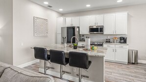 A modern kitchen with white cabinets, stainless steel appliances, and a marble island with bar stools. - Movie Theater/Game Room, FREE Pool Heat! No Rear Neighbors, Minutes to Disney! (Kissimmee)