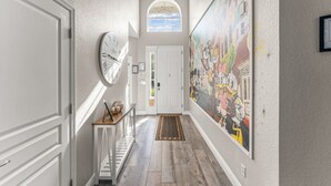 A hallway with a large mural, a clock, and a door at the end. - Movie Theater/Game Room, FREE Pool Heat! No Rear Neighbors, Minutes to Disney! (Kissimmee)