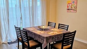 A dining area with a square table covered by a patterned tablecloth, surrounded by four wooden chairs with cushioned seats. - Luxury 5BD 4BR Sleep 12 - Large Groups, Family, Events , Wedding near Brantford (Brant)