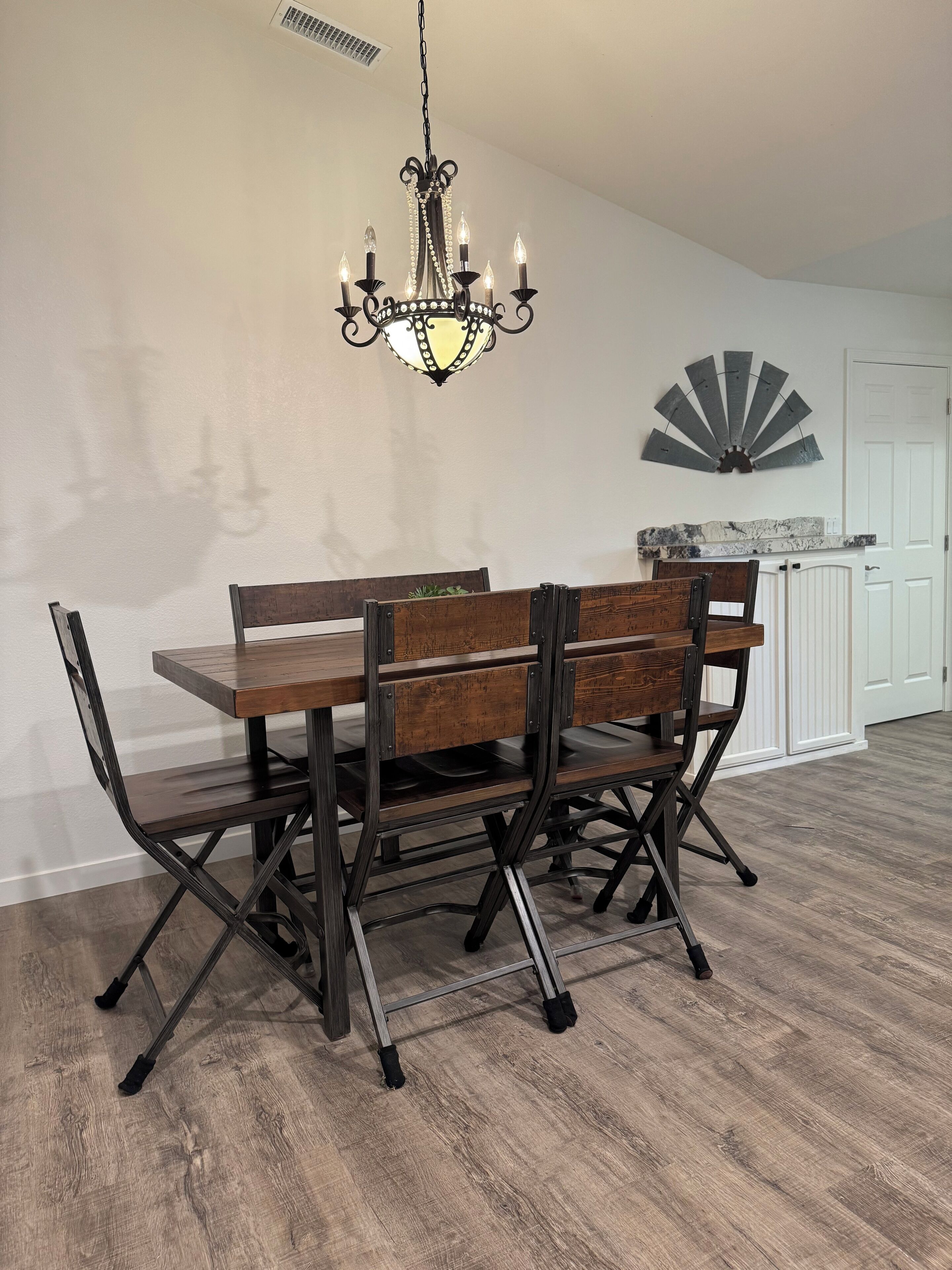 A dining area with a wooden table and chairs, a chandelier, and a decorative fan on the wall.